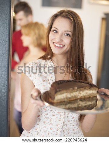Portrait of happy woman holding cake in tray with friends in background at cafe