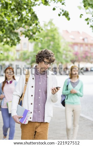 Young male student using cell phone with friends in background on street