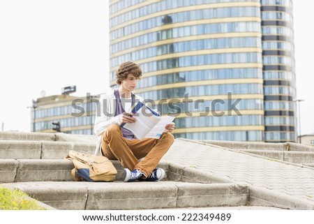 Full length of young male college student reading book against building