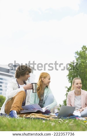 Young man having coffee while studying with female friends at college campus