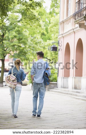Full length rear view of young college friends talking while walking in campus