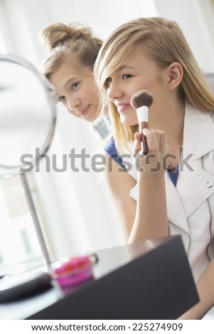 Girl watching sister applying makeup in front of mirror at home