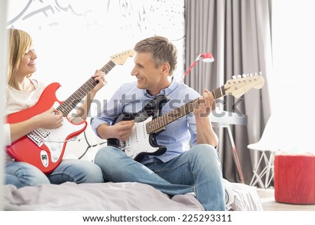 Happy father and daughter playing guitars at home
