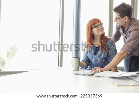 Businesspeople looking at each other while working at desk in creative office