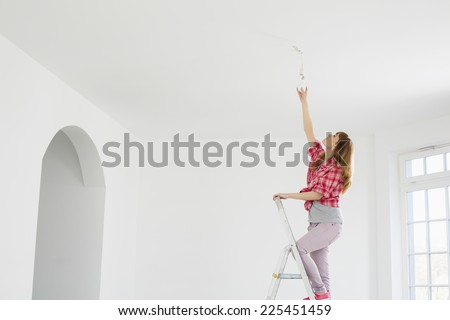 Full-length of woman on ladder fitting light bulb in new house