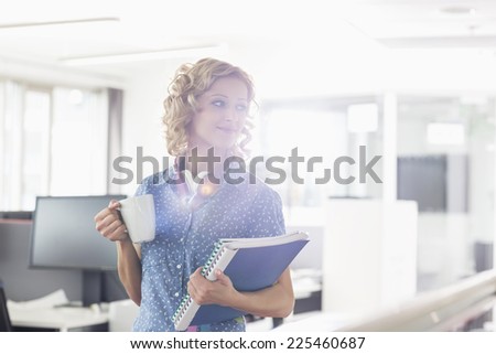 Businesswoman having coffee while holding files in creative office