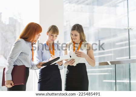 Businesswomen doing paperwork by railing in office