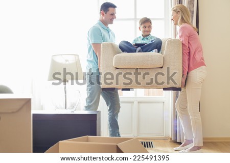 Parents carrying son on armchair in new house