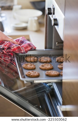 Cropped image of woman's hand removing cookie tray from oven in kitchen