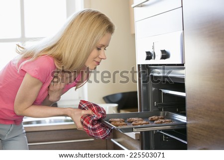 Mid adult woman removing baking tray from oven in kitchen