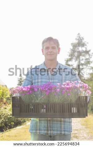 Portrait of man carrying crate with flower pots in garden