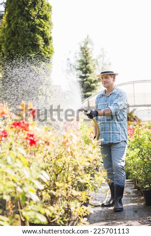 Full-length of man watering plants outside greenhouse