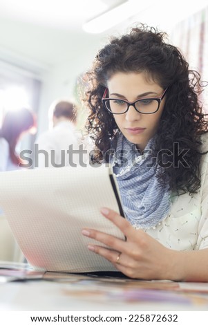 Young businesswoman reading notepad at creative office with colleagues in background