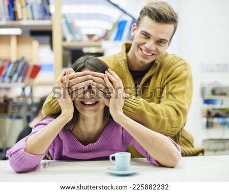 Playful young man covering woman\'s eyes in library