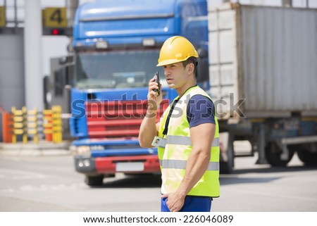 Mid adult man using walkie-talkie in shipping yard
