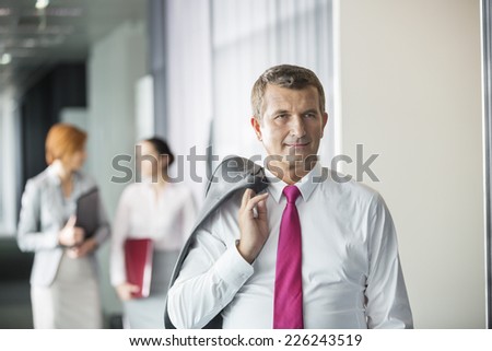 Businessman holding coat over shoulder with female colleagues in background at office