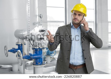Serious young male manager using cell phone in industry