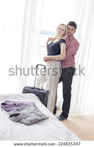 Portrait of young man embracing woman from behind in hotel room