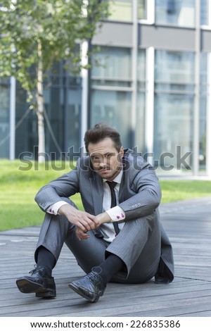 Full length portrait of stressed businessman sitting on path outside office