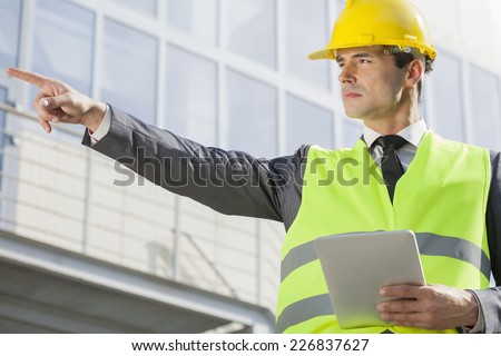 Young male engineer with digital tablet pointing away outside industry