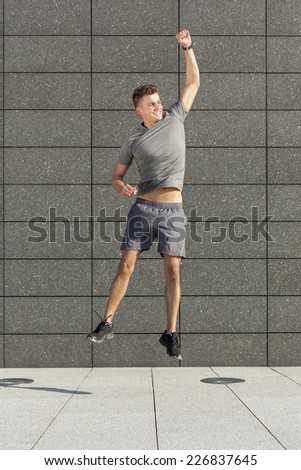 Full length of excited runner jumping against tiled wall