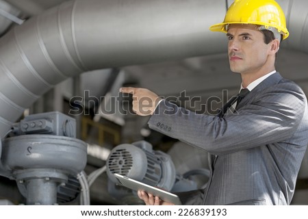 Confident young male manager with digital tablet pointing at machinery in industry