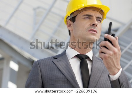 Young male architect talking on two-way radio outdoors