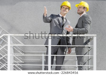 Two young businessmen in hard hats discussing on stairway