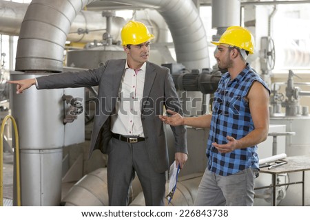 Serious manager showing something to worker in industry