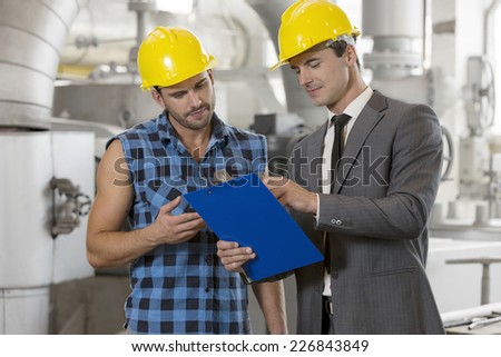 Worker with manager discussing over clipboard in industry