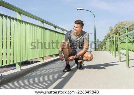 Full length of male jogger tying shoelace on bridge