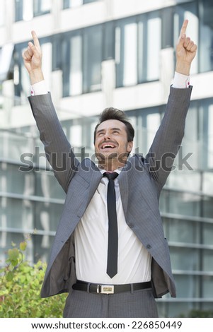Successful businessman pointing upwards outside office building