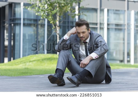 Full length of depressed businessman sitting on path outside office