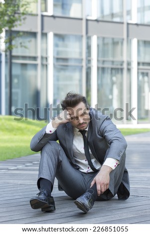Full length of stressed businessman sitting on path outside office