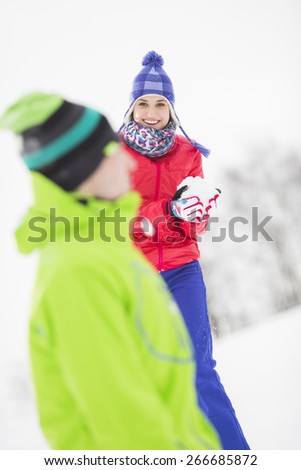 Smiling young woman having snowball fight with male friend