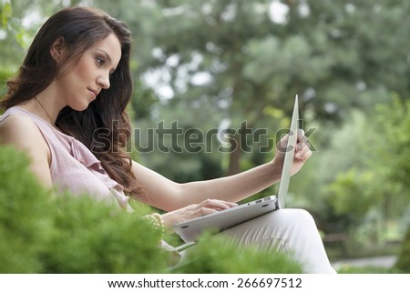 Side view of beautiful young woman using laptop in park
