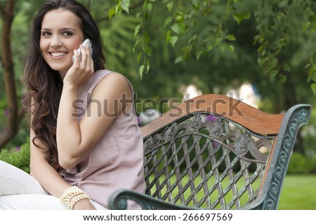 Beautiful young woman using cell phone on bench in park
