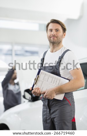 Portrait of confident male automobile mechanic with clipboard in car repair store