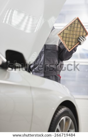 Midsection of male maintenance engineer repairing car in automobile store