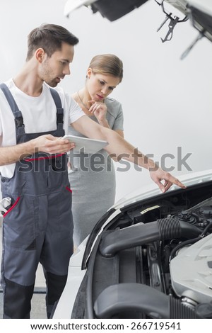 Young repair worker explaining car engine to worried customer in workshop
