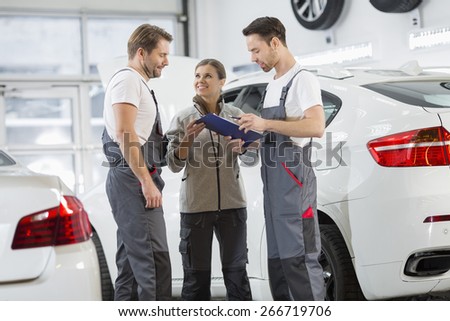 Automobile mechanics discussing over clipboard in car repair shop