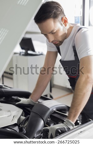 Full length side view of male mechanic examining car engine in repair shop