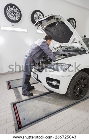Full length side view of male automobile mechanic repairing car engine in repair shop