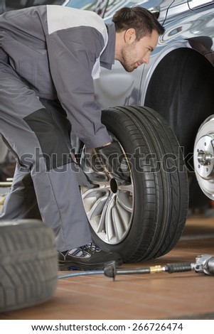 Full length of male mechanic fixing car\'s tire in repair shop