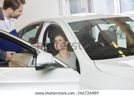 Female customer receiving car key from mechanic in automobile repair shop