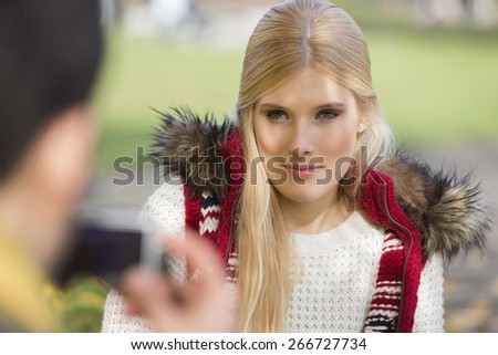 Beautiful young woman being photographed by man in park