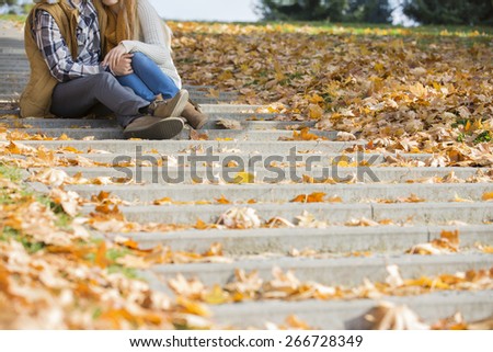 Low section of couple sitting on steps in park during autumn
