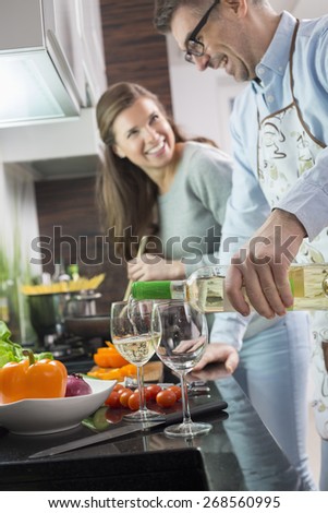 Man pouring white wine in glasses while cooking with woman at kitchen