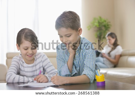 Siblings drawing together at table with mother in background
