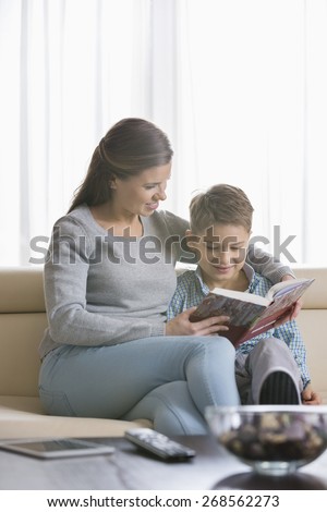 Mother and son reading book on sofa at home